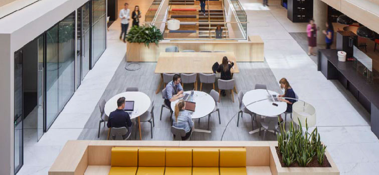 Authorisations image A common area inside the main Central Bank of Ireland offices with a yellow sofa and three round tables with four people seated and looking at laptops are in the foreground. A table, five people and stairs are the background area.
